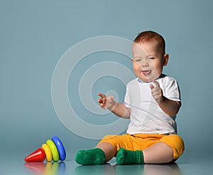 Laughing sneezing Infant baby boy toddler is playing with a children multi-colored developing pyramid fallen on floor