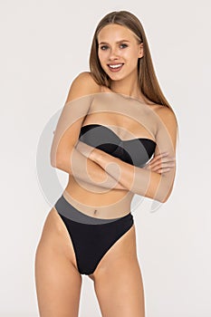 Laughing sporty woman in black bikini posing on grey background. Attractive girl with slim toned body. Beauty and body care