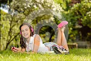 Laughing student girl with headphones lying grass