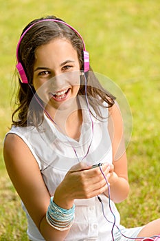 Laughing teenage girl listen music sitting grass