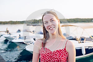 Laughing teenage girl in a red summer dress against a background of blurry motorboats mooring in the port - shallow depth of field