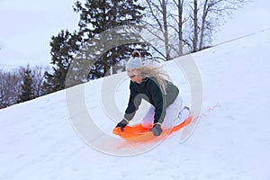 A laughing teenage girl,sliding down a winte hill