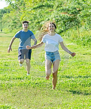 Laughing teenagers playing outdoors funning at grass on day