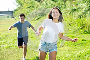 Laughing teenagers playing outdoors funning at grass on day