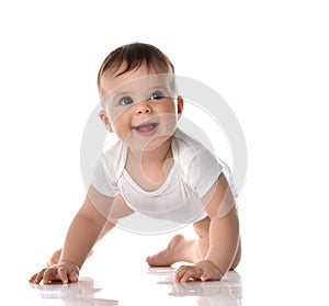 Laughing toddler baby in diaper and white bodysuit is crawling on floor and looking up at the corner trying to stand up