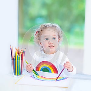 Laughing toddler girl drawing next to window