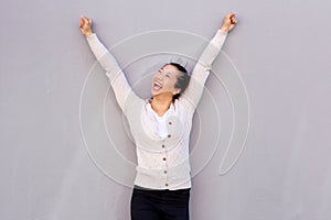 Laughing woman with arms raised against gray background