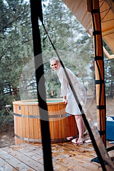 Laughing woman in bathrobe at the font for bathing in the forest. hot tub