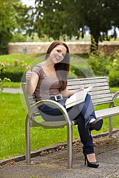 Laughing woman with book posing thumbs up