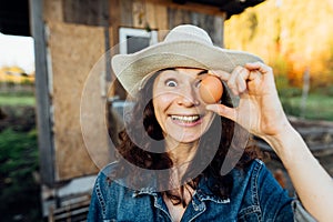 Laughing Woman in Hat Holds Egg to Face, Closing Eye