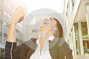 Laughing woman holding smart phone with earphones