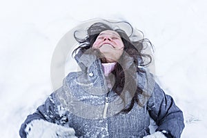 Laughing woman lies on the snow. Pretty brunette enjoys winter. Top view