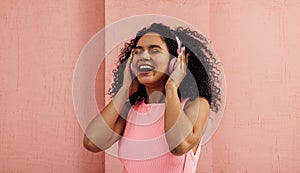 Laughing woman listening to music with pink headphones with closed eyes. Young happy female in pink casuals enjoying music