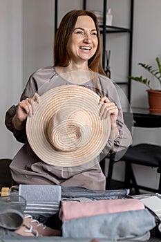 Laughing woman posing with straw hat packing baggage getting ready to travel vacation konmari method