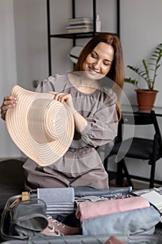 Laughing woman posing with straw hat packing baggage getting ready to travel vacation konmari method