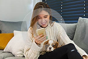 Laughing woman sits with her dog on her lap and looks at the phone