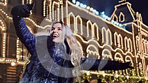 Laughing woman taking selfie using smartphone at illuminating Christmas facade house background