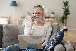 Laughing woman talking on phone, sitting on couch, using laptop