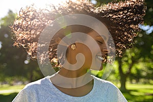 Laughing woman twirling her curly hair outside in a park