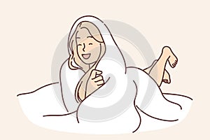 Laughing woman wrapped in blanket lies on bed not wanting to get up and go to work or college