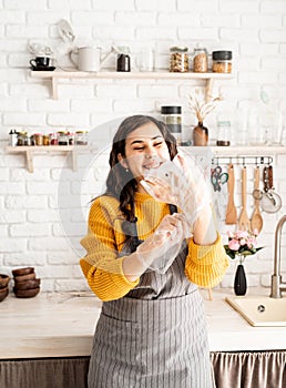 Laughing woman in yellow sweater and gray apron preparing to color easter eggs in the kitchen putting on the gloves