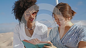 Laughing women reading book on beach closeup. Love partners enjoying summer