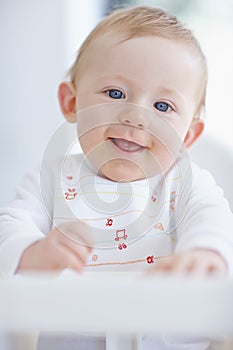 Laughing at you. A cute baby boy smiling while sitting in his high chair.