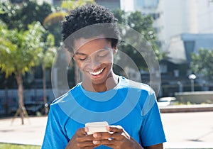 Laughing young african american man sending message with mobile