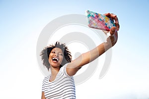 Laughing young african american woman taking selfie with smart phone outdoors