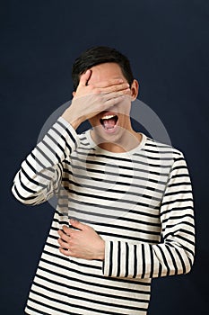 Laughing young Asian man covering his face by palm