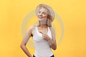 Laughing young beautiful woman in t-shirt looking and pointing away with finger over yellow background