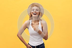 Laughing young beautiful woman in t-shirt looking and pointing away with finger over yellow background