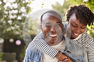 Laughing young black couple piggyback in garden, to camera