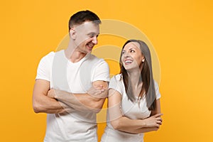 Laughing young couple two friends guy girls in white blank empty design t-shirts posing isolated on yellow orange wall