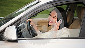 Laughing young elegant business executive woman recieves a call on phone in car