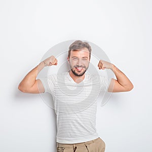 Laughing young fit casual man flexing his muscles