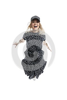 A laughing young girl in a black dress, a cap and white sneakers is jumping. Freedom and relaxation. Isolated on white background