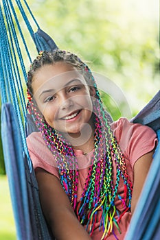 Laughing young girl with colorful braids is posing on hammock