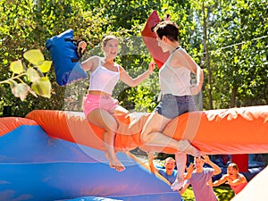 Laughing young girl fighting by pillows with female opponent on inflatable beam