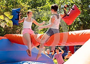 Laughing young girl fighting by pillows with female opponent on inflatable beam