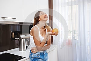 Laughing young girl holding orange at kitchen
