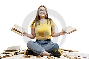 A laughing young girl in jeans and a blue T-shirt sits on a pile of opened books and holds books in her hands. Education and