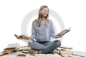 A laughing young girl in jeans and a blue T-shirt sits on a pile of opened books and holds books in her hands. Education and