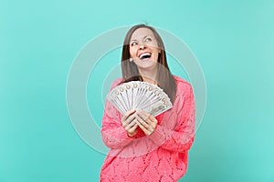 Laughing young girl in knitted pink sweater looking up hold in hand lots bunch of dollars banknotes cash money isolated