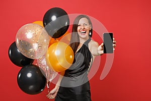 Laughing young girl in little black dress celebrating holding mobile phone with blank black empty screen, air balloons