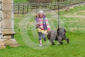 Laughing young girl running with black labradoodle dog in a rural setting