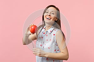 Laughing young girl in summer clothes holding fresh ripe red apple fruit glass cup isolated on pink pastel wall