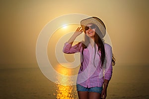 Laughing young girl in summer hat and sunglasses overlooking beautiful sunset. Rest on the sea, travel, happy life