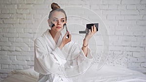 Laughing young girl with a towel on her head puts a black mask on her face, day spa