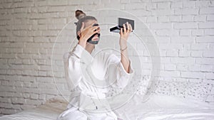 Laughing young girl with a towel on her head puts a black mask on her face, day spa